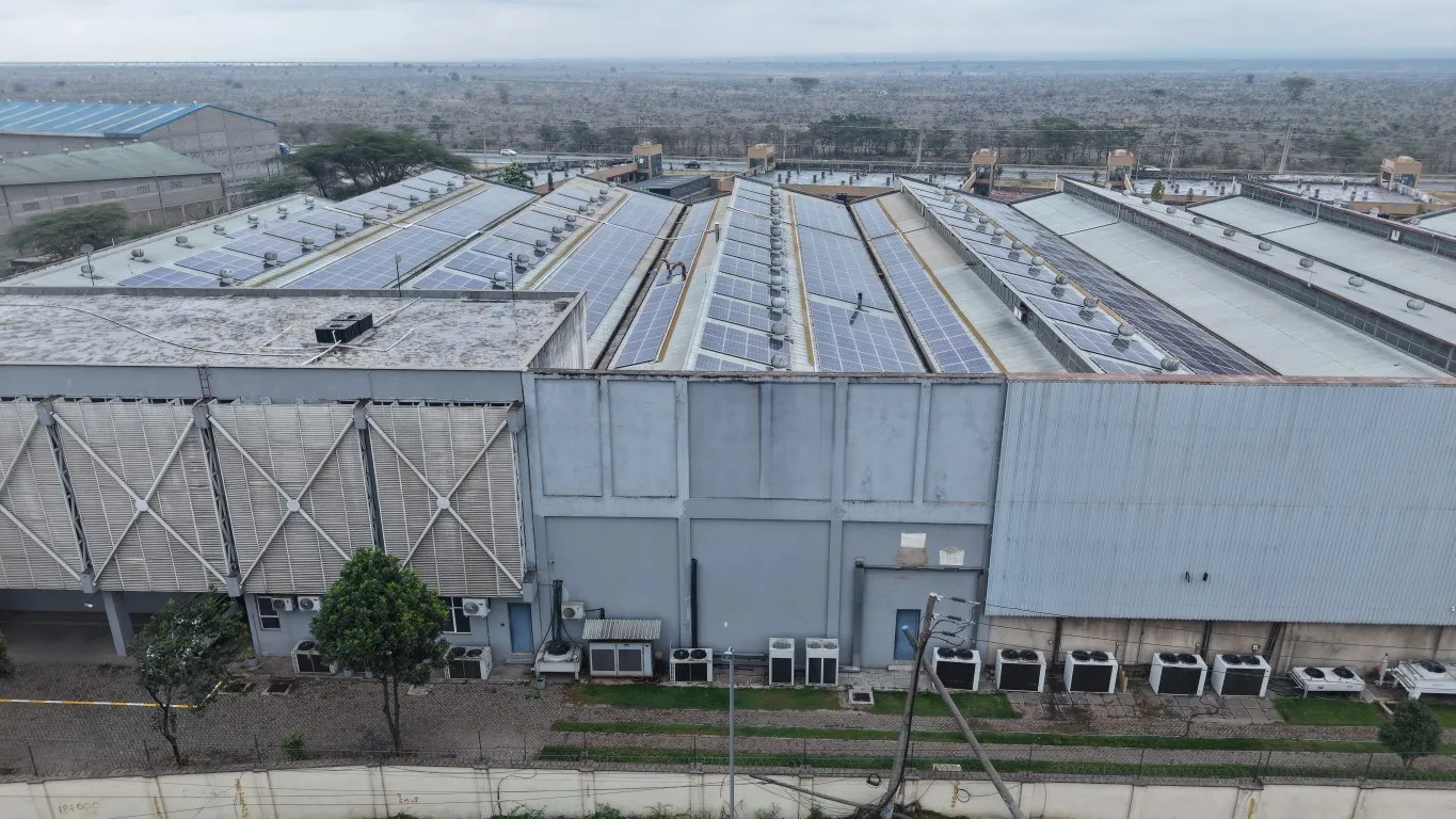 Side aerial view of an industrial printing and assembly factory with rooftop solar panels along its roof bays