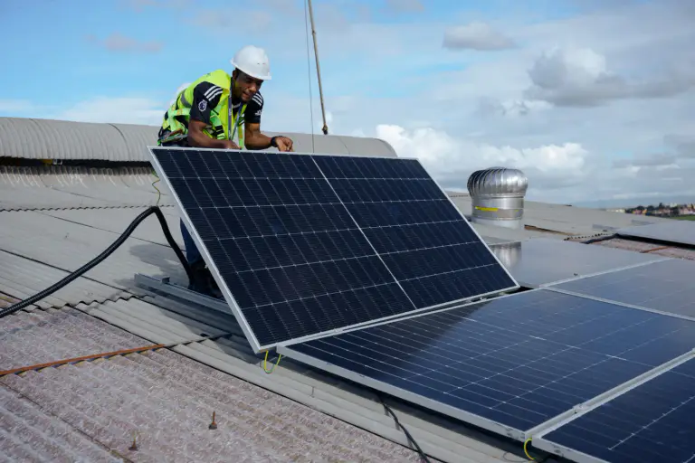 Technician in a safety harness installing solar panels on a factory roof